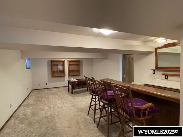 dining room with light colored carpet, a bar, and baseboards