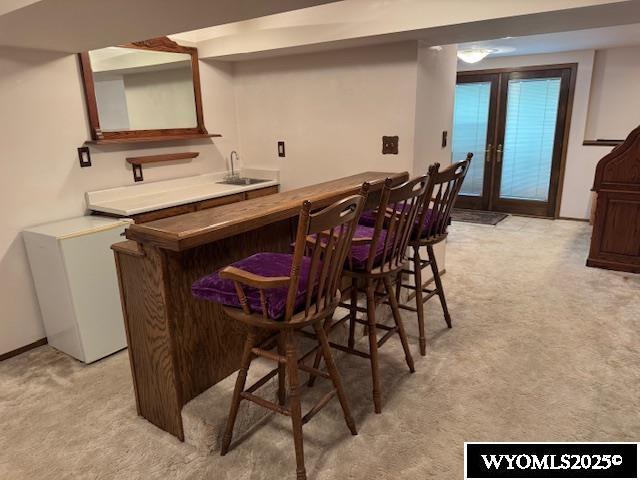 indoor wet bar with fridge, french doors, and light colored carpet