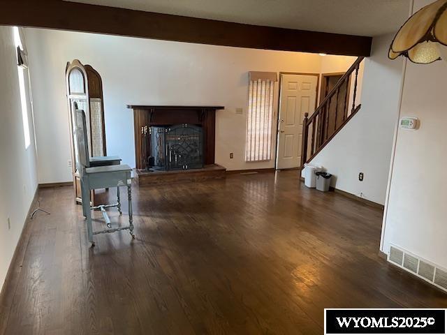 unfurnished living room with wood finished floors, stairway, a fireplace with raised hearth, and baseboards
