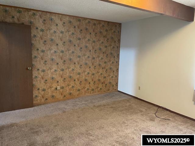 carpeted empty room with wallpapered walls, a textured ceiling, and baseboards