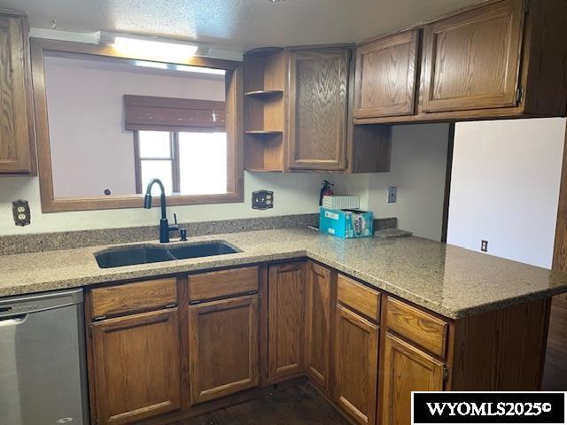 kitchen featuring stainless steel dishwasher, a sink, a peninsula, open shelves, and brown cabinetry
