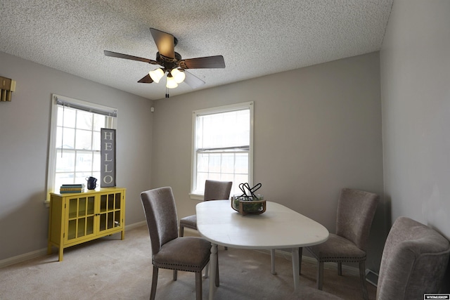 dining space featuring a ceiling fan, a textured ceiling, light colored carpet, and baseboards