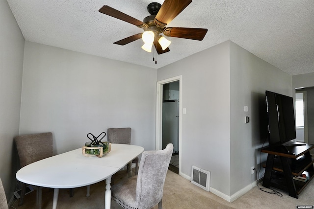 dining room featuring light carpet, ceiling fan, a textured ceiling, and baseboards