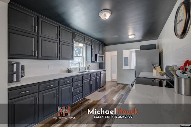 kitchen with appliances with stainless steel finishes, a sink, tasteful backsplash, dark wood-type flooring, and light countertops