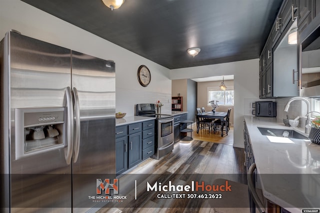 kitchen with stainless steel appliances, a sink, dark wood finished floors, decorative backsplash, and blue cabinetry