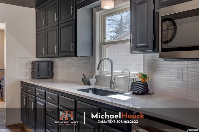 kitchen with stainless steel microwave, a sink, backsplash, and wood finished floors