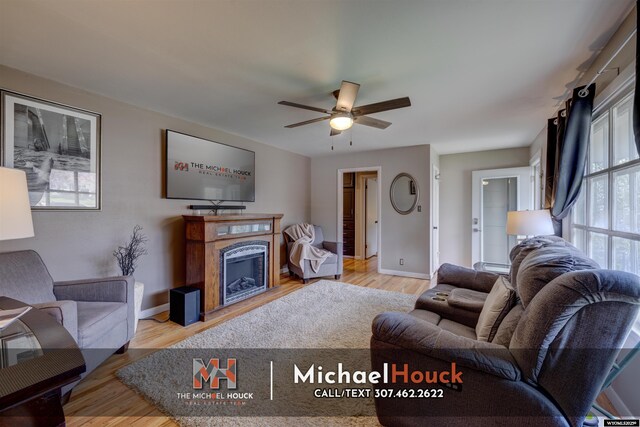 living area with wood finished floors, a ceiling fan, a fireplace, and baseboards