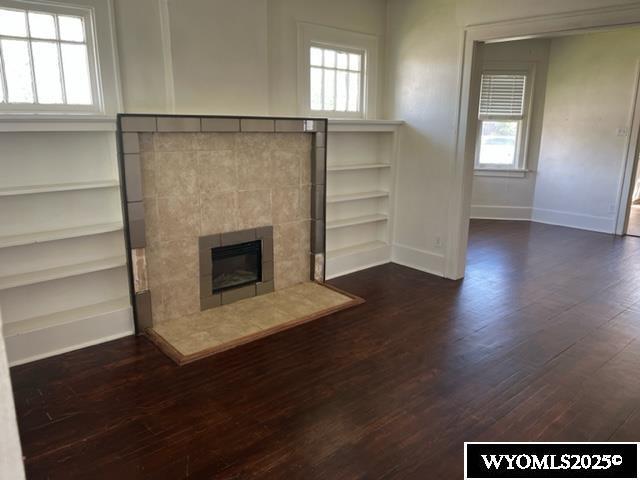 unfurnished living room featuring baseboards, dark wood finished floors, plenty of natural light, and a tile fireplace