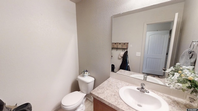 bathroom with toilet, vanity, and a textured wall