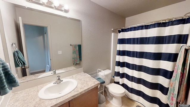 bathroom featuring a textured wall, vanity, toilet, and a shower with curtain