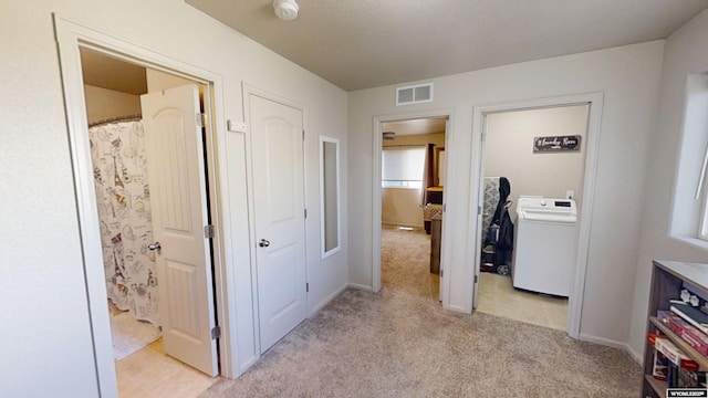 corridor with washer / clothes dryer, light colored carpet, and baseboards