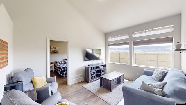 living room featuring high vaulted ceiling, light wood-type flooring, and baseboards
