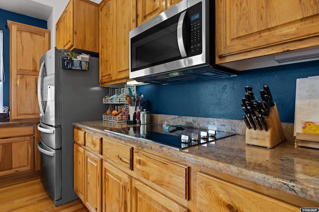 kitchen featuring stainless steel appliances, light wood-type flooring, stone counters, and brown cabinets