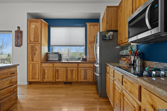 kitchen with appliances with stainless steel finishes, light wood finished floors, brown cabinetry, and dark countertops