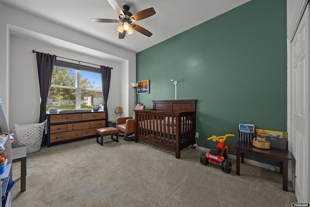 carpeted bedroom featuring a nursery area and a ceiling fan