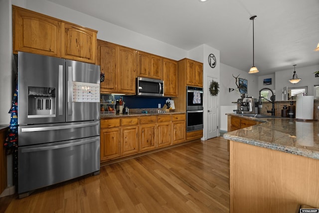 kitchen with stainless steel appliances, a sink, wood finished floors, brown cabinets, and dark stone counters