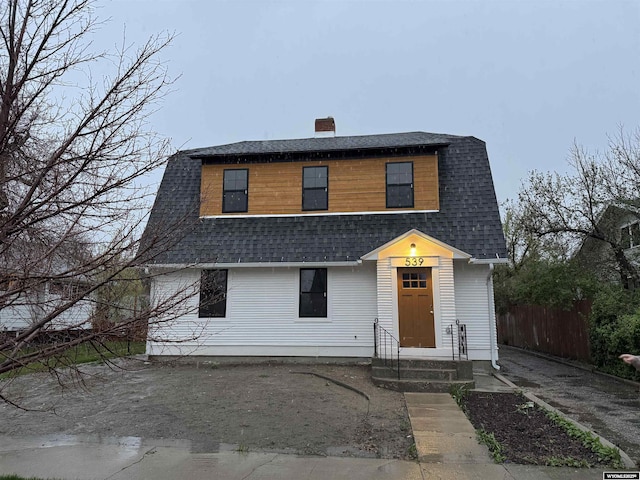 dutch colonial with a chimney, roof with shingles, and fence