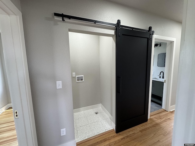 washroom with a barn door, wood finished floors, washer hookup, and baseboards
