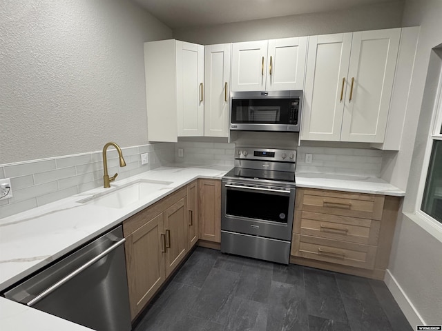 kitchen featuring appliances with stainless steel finishes, a sink, light stone counters, white cabinetry, and decorative backsplash