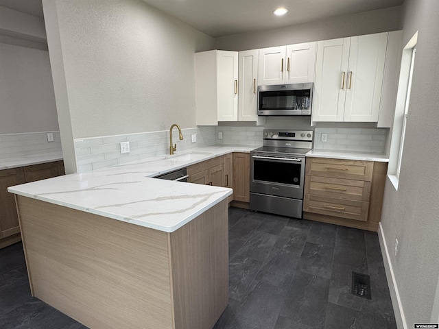 kitchen featuring appliances with stainless steel finishes, a sink, decorative backsplash, a peninsula, and recessed lighting