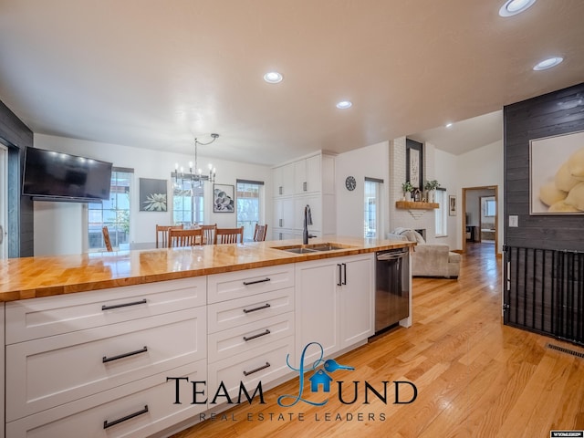 kitchen with dishwasher, butcher block countertops, a sink, a chandelier, and a brick fireplace