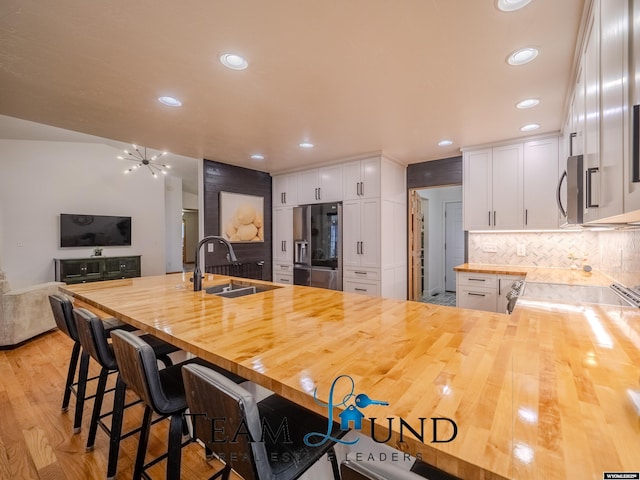 kitchen with butcher block countertops, stainless steel appliances, a sink, white cabinetry, and recessed lighting