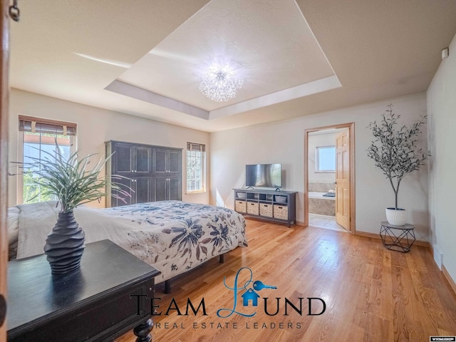 bedroom with multiple windows, wood finished floors, baseboards, and a tray ceiling