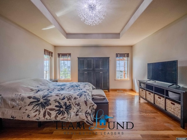 bedroom with a tray ceiling, wood finished floors, and baseboards