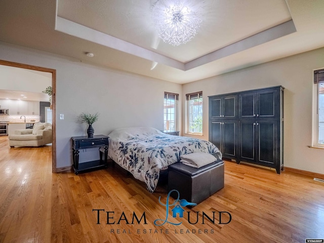 bedroom with a raised ceiling, light wood-style floors, a sink, and baseboards