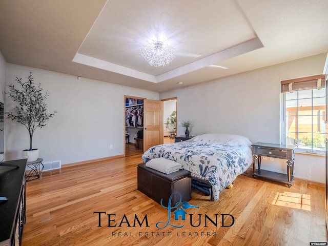 bedroom with a raised ceiling, light wood-type flooring, baseboards, and a spacious closet