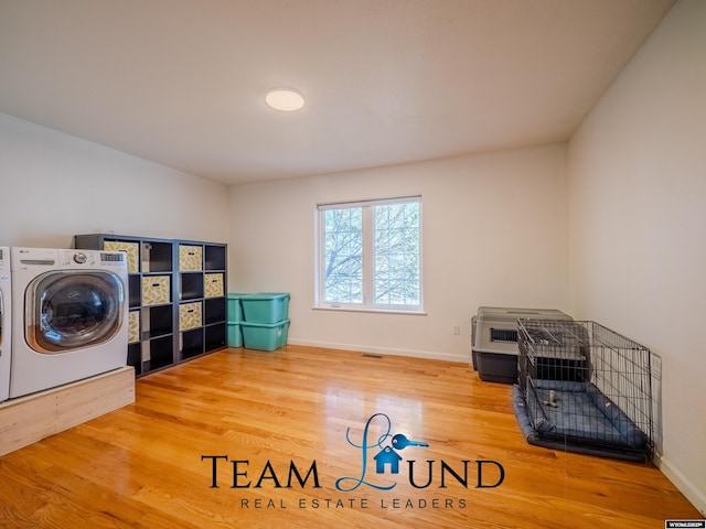 clothes washing area with wood finished floors, independent washer and dryer, and baseboards