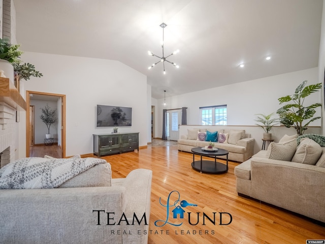 living area featuring vaulted ceiling, a brick fireplace, a chandelier, wood finished floors, and baseboards