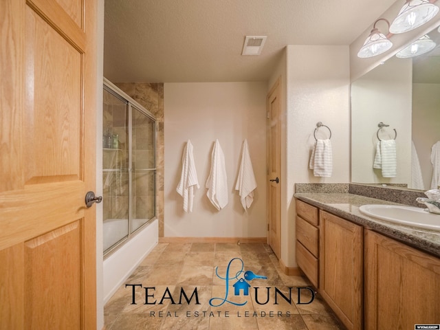 bathroom with vanity, bath / shower combo with glass door, a textured ceiling, and baseboards