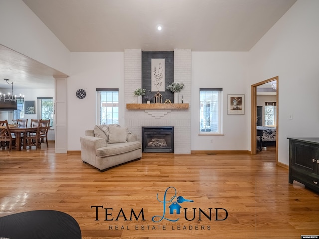 living room with a brick fireplace, light wood-style floors, a chandelier, and baseboards