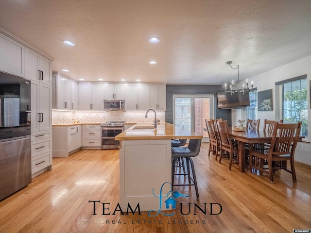 kitchen featuring stainless steel appliances, light wood-style flooring, a sink, decorative backsplash, and a kitchen breakfast bar