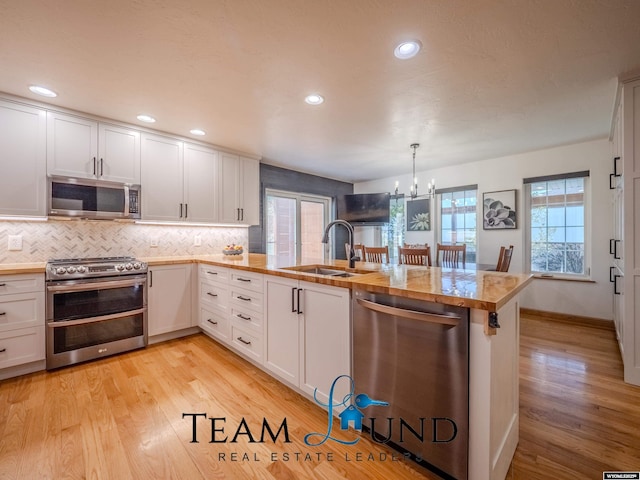 kitchen with appliances with stainless steel finishes, a sink, a peninsula, a chandelier, and white cabinetry