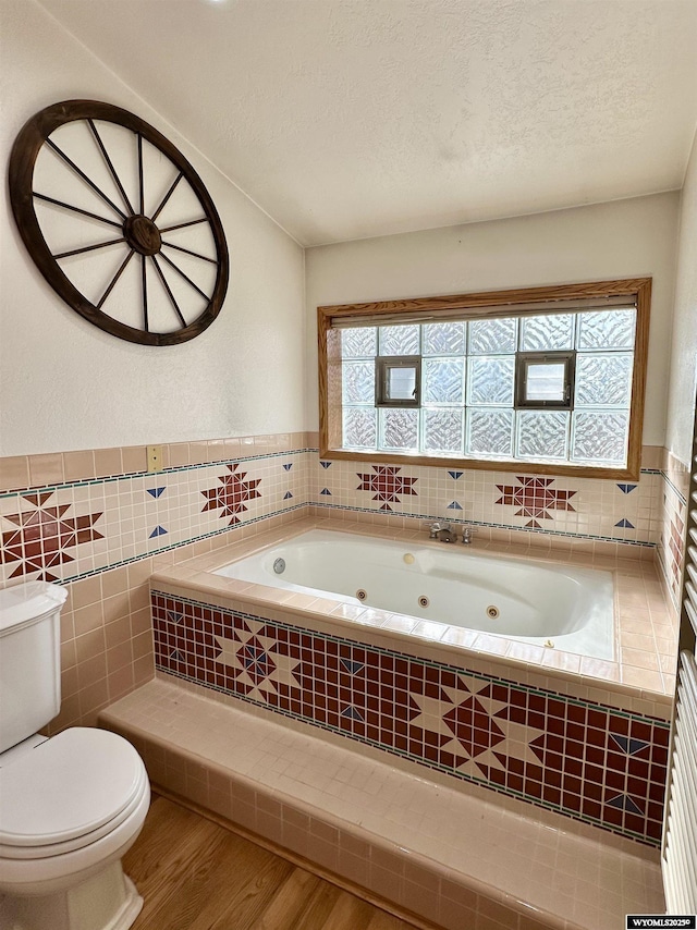 920 Laramie St, Rock Springs, WY 82901 - bathroom with toilet, wood finished floors, a jetted tub, a textured ceiling, and tile walls