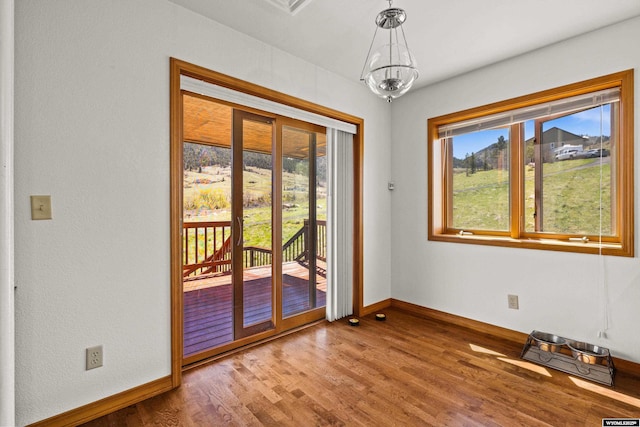 doorway to outside featuring baseboards, wood finished floors, and a chandelier