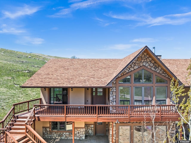 view of front of property with stone siding, a shingled roof, stucco siding, and a wooden deck
