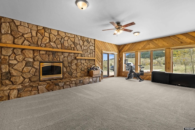 unfurnished living room featuring carpet, ceiling fan, a fireplace, and wooden walls