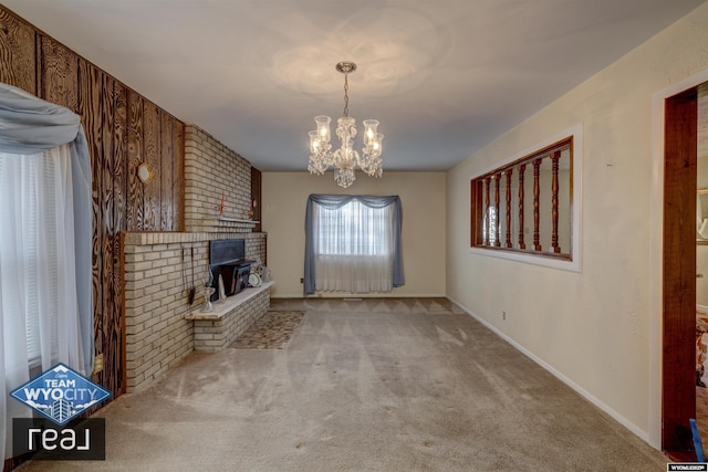 unfurnished living room featuring carpet, a chandelier, a brick fireplace, and baseboards