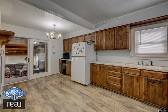 kitchen with freestanding refrigerator, a sink, light countertops, beamed ceiling, and light wood-type flooring