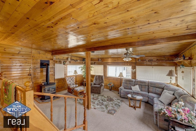 carpeted living area featuring a wood stove, ceiling fan, wood ceiling, and wood walls