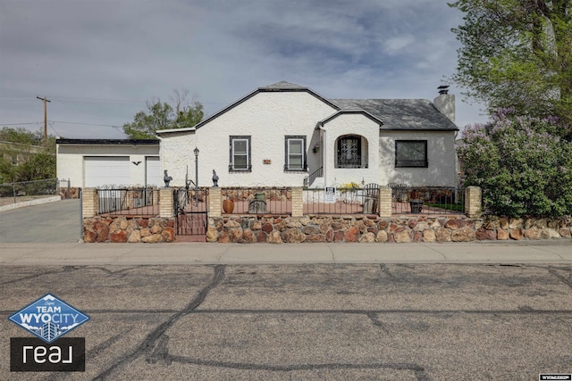view of front of home featuring a fenced front yard, a chimney, a garage, driveway, and a gate