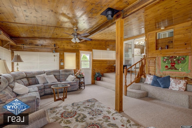 carpeted living area featuring wood walls, wooden ceiling, stairs, and a ceiling fan
