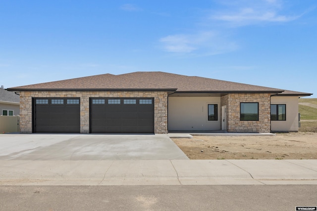 prairie-style home with stone siding, a garage, concrete driveway, and roof with shingles