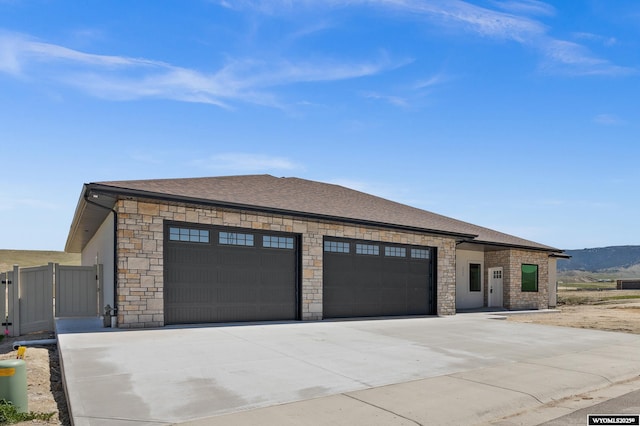 view of front of property featuring an attached garage, driveway, stone siding, and roof with shingles