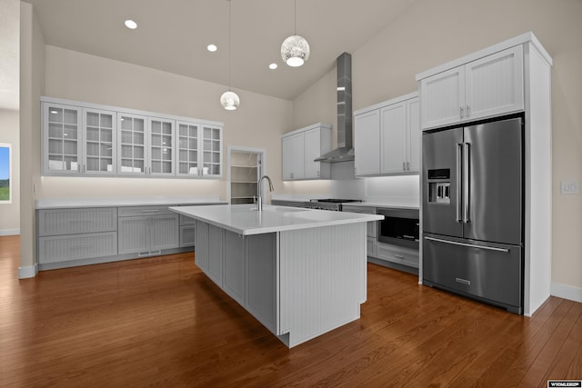 kitchen with high quality fridge, wall chimney exhaust hood, glass insert cabinets, high vaulted ceiling, and dark wood-type flooring