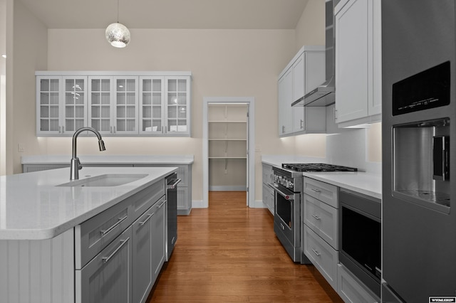 kitchen with high end stainless steel range, a sink, wall chimney range hood, wood finished floors, and glass insert cabinets