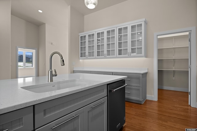 kitchen with a sink, gray cabinetry, light stone counters, glass insert cabinets, and dark wood-style flooring